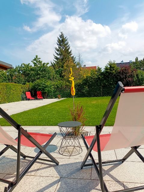 Zwei Liegestühle im Garten mit Rasen und Bäumen im Hintergrund.