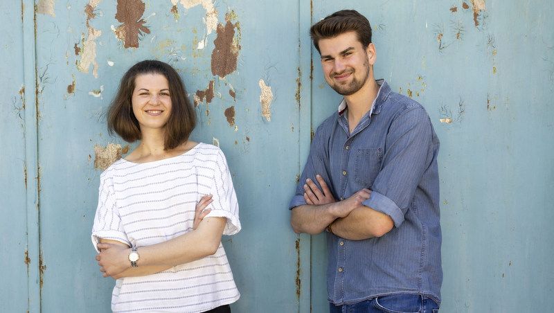 Zwei Personen stehen vor einer blauen, abgenutzten Wand.