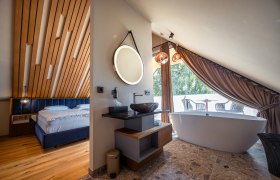 Modernes Hotelzimmer mit Holzdecke, freistehender Badewanne und Balkon.