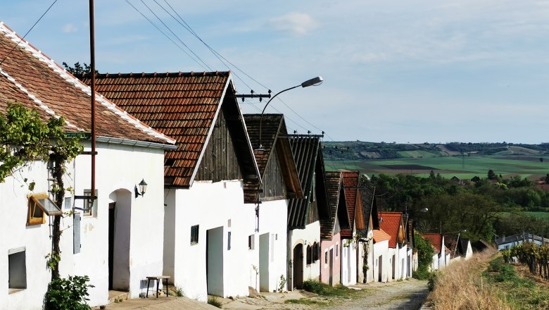 Reihe von Weinkellern in Haugsdorf mit roten D&auml;chern und wei&szlig;er Fassade, umgeben von gr&uuml;ner Landschaft.
