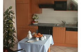 Kleine Küche mit Holzmöbeln, Esstisch mit blauer Tischdecke und Geschirr.