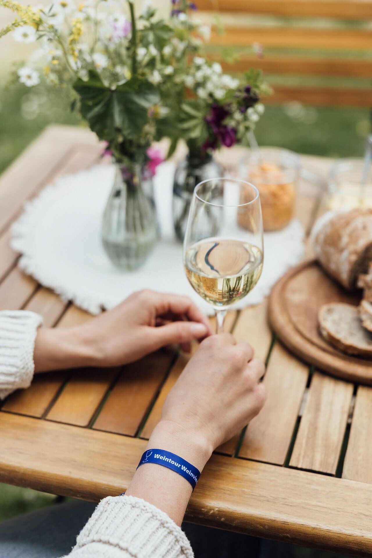 Ein sonniger Nachmittag auf einem malerischen Winzerhof, wo die Gäste mit einem Glas frischem Wein anstoßen. Umgeben von blühenden Wildblumen und einer einladenden Jause, genießen die Besucher die entspannte Atmosphäre und die köstlichen Aromen der Region.