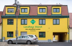 Gelbes Gebäude mit der Aufschrift 'Landhaus Storch', davor geparkte Autos.