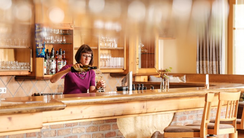 A woman stands behind a bar in a rustic restaurant and pours wine.