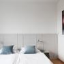 A simple guest room with a double bed, blue cushions, white walls and a picture on the wall.