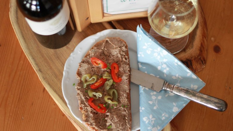 A plate with spread, peppers and a knife, next to it a glass of white wine and a bottle of wine on a wooden table.