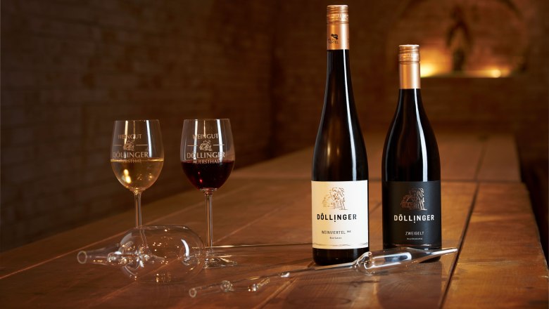 Zwei Weingläser und zwei Flaschen Wein auf einem Holztisch in einem Weinkeller.