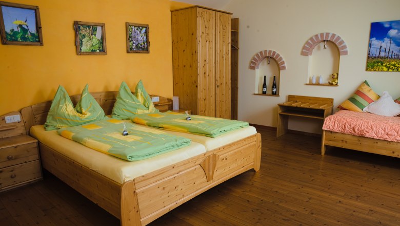 Gemütliches Gästezimmer mit Holzmöbeln, Doppelbett, Einzelbett und dekorativen Bildern an der Wand.