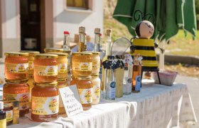 Honiggläser und Flaschen auf einem Tisch mit einer Bienenfigur im Hintergrund.