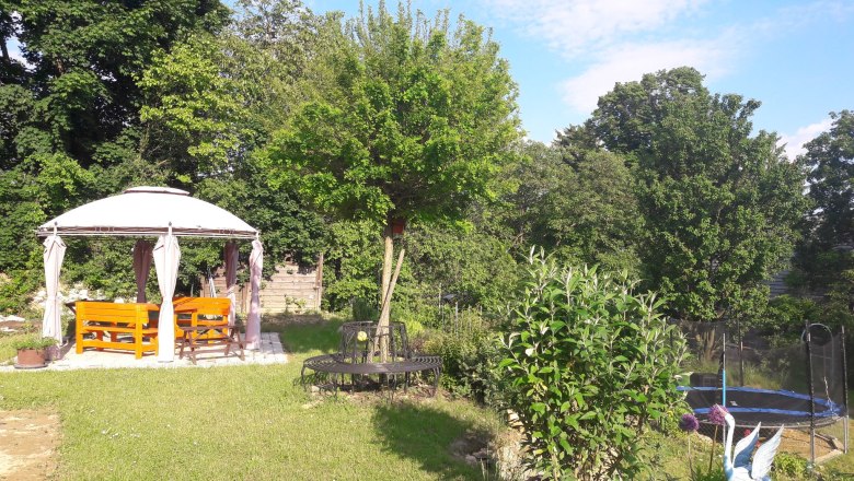 Ein Garten mit Pavillon, Bänken, Trampolin und Bäumen.