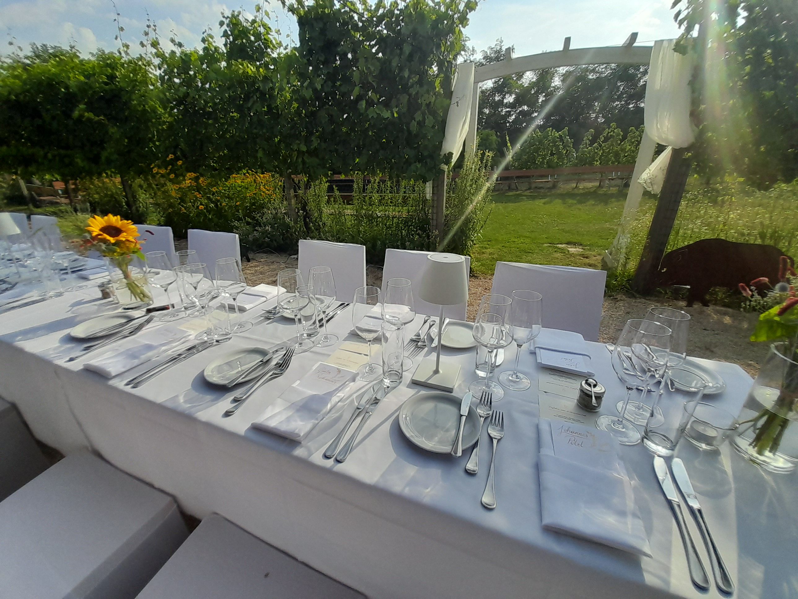 Elegante, gedeckte Tafel im Freien mit weißen Tischdecken und Sonnenblume als Dekoration.