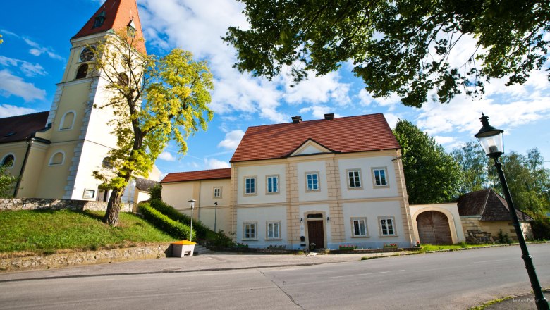 Pfarrhof Zuschmann mit Kirche und blauem Himmel.
