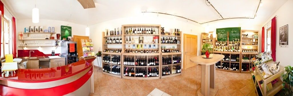 Innenansicht eines Weinladens mit Regalen voller Weinflaschen und einem roten Tresen.