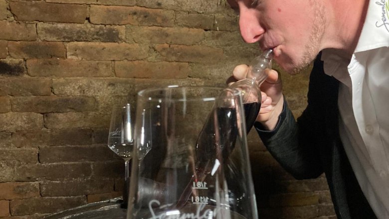 Ein Mann probiert Wein aus einer Pipette in einem Weinkeller.