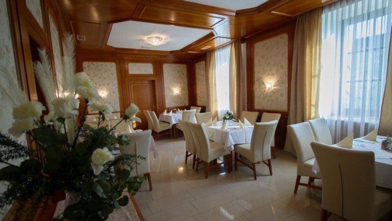 Eleganter Speisesaal mit gedeckten Tischen, weißen Stühlen und Blumenarrangement.