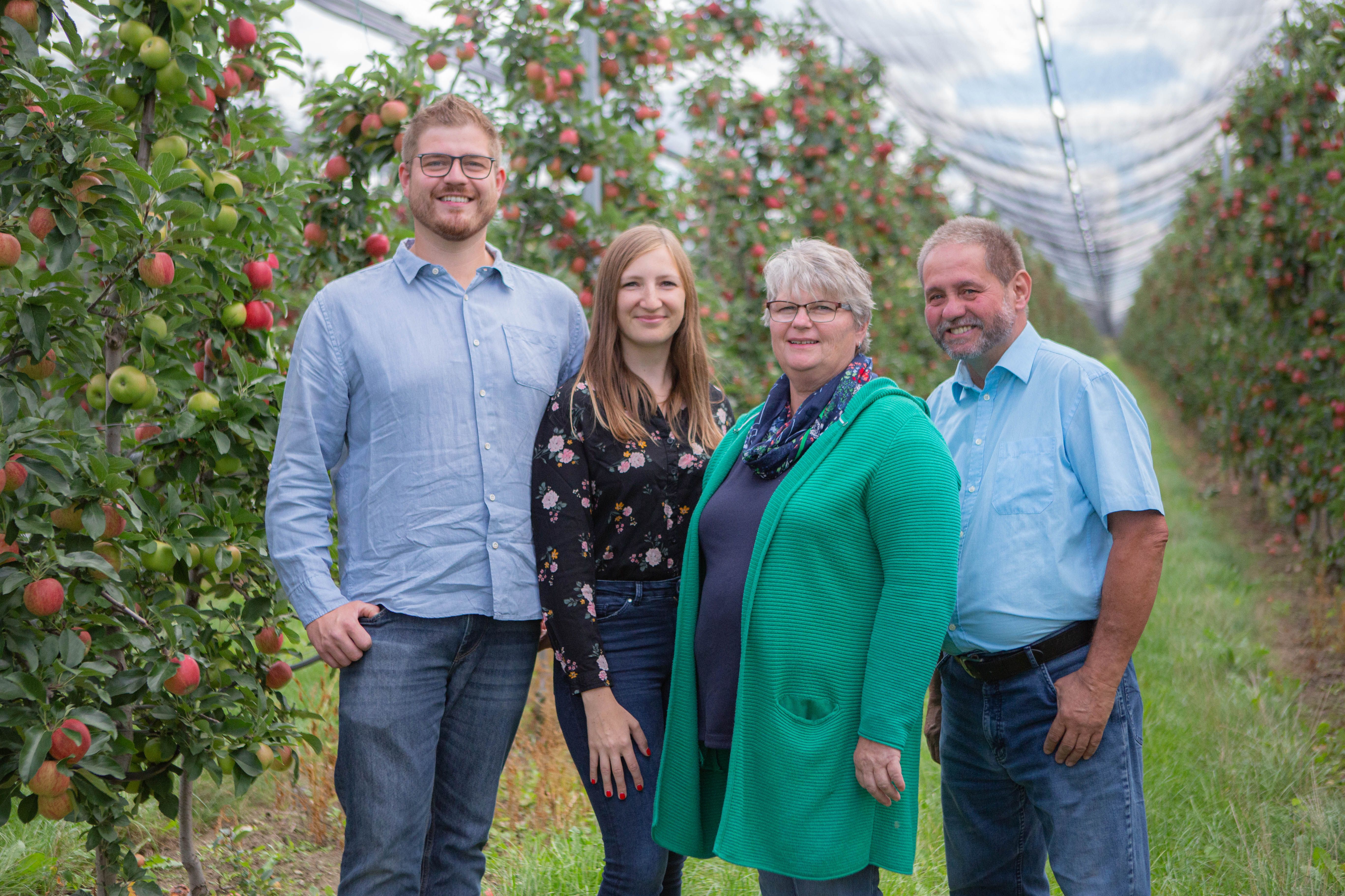 Vier Personen stehen in einer Apfelplantage.