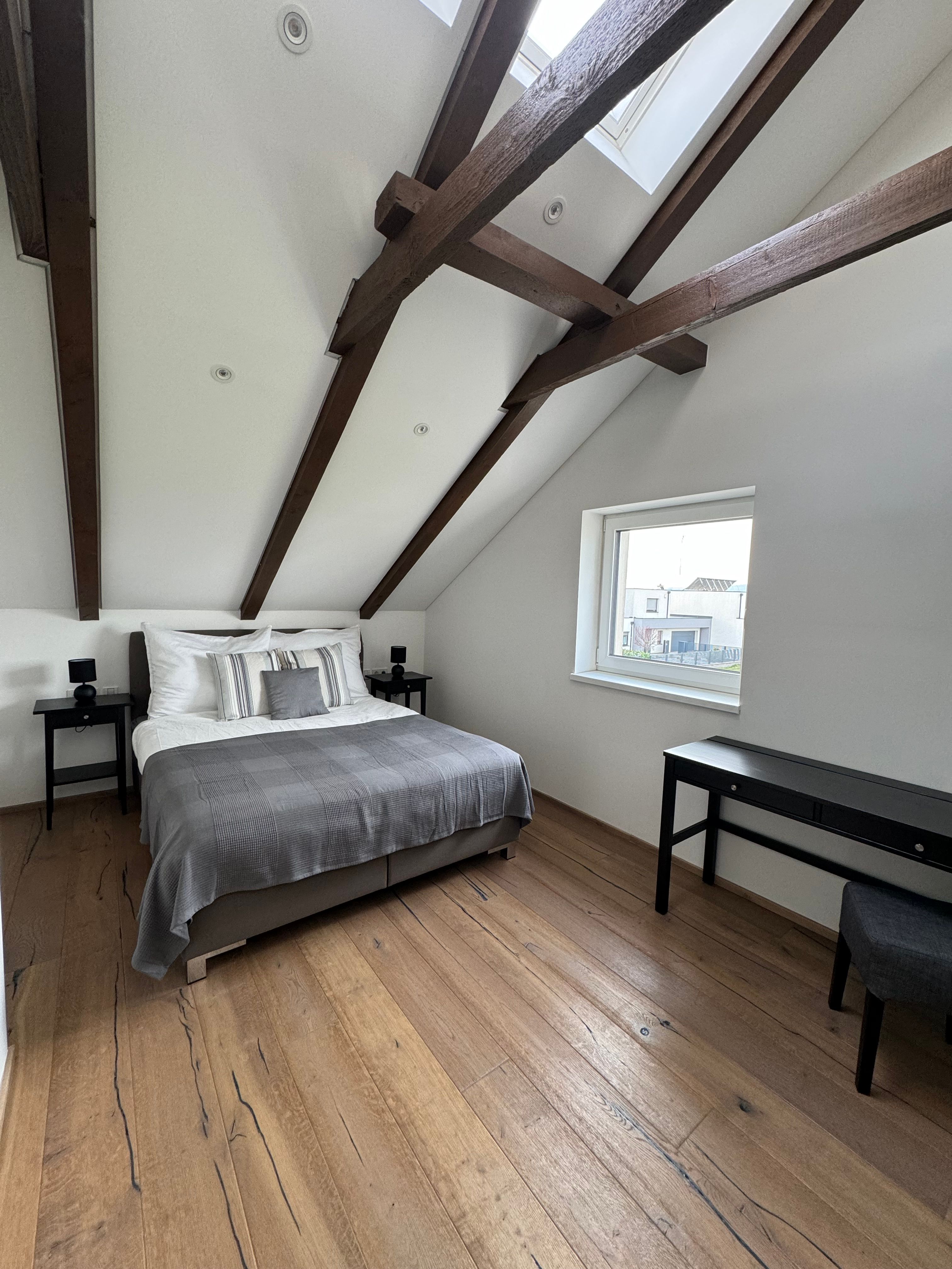 Modernes Schlafzimmer mit Holzbalkendecke, Doppelbett, Holzboden und Fenster.