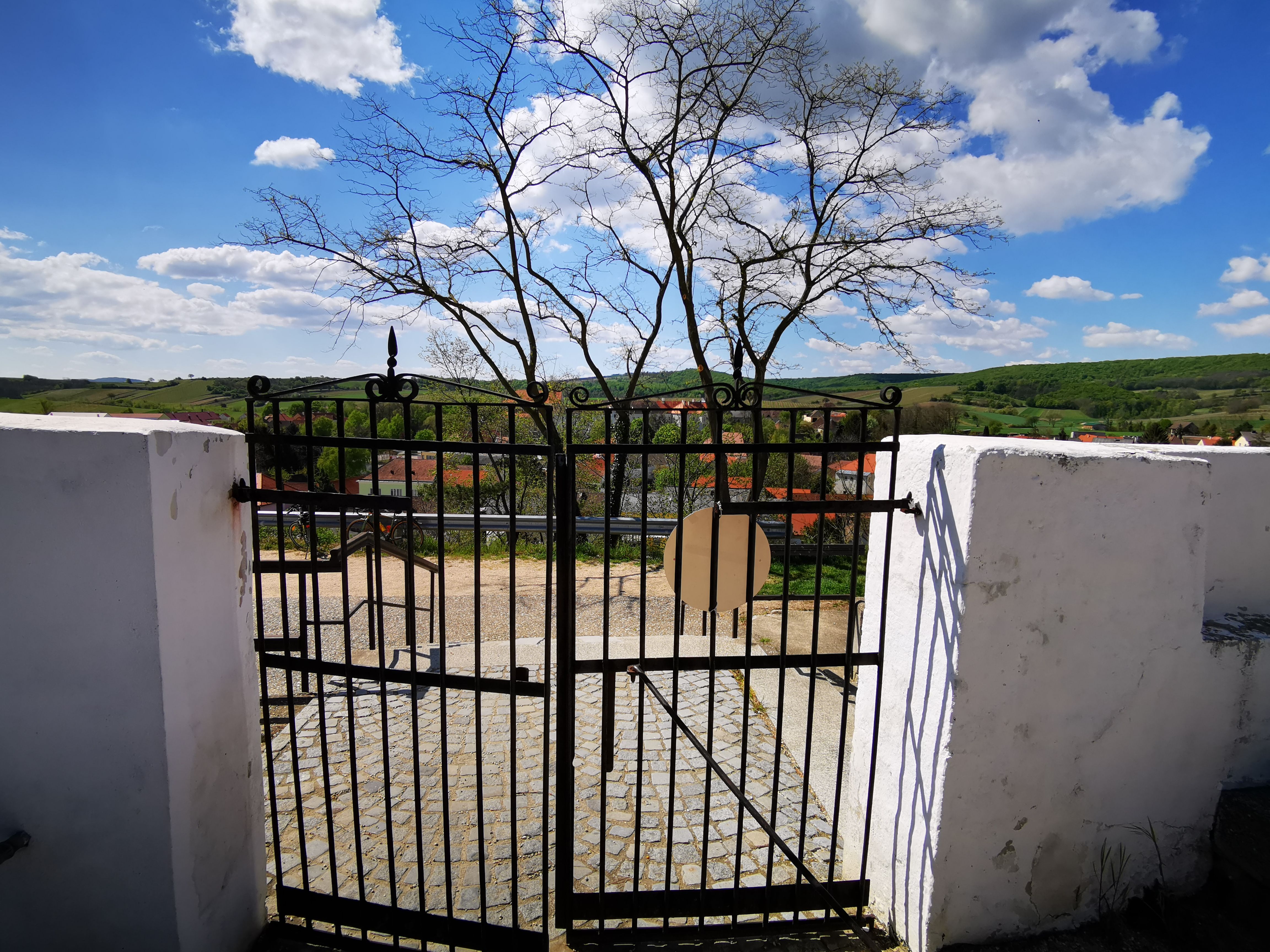 Friedhofstor aus Eisen mit Blick auf Landschaft und Dorf.