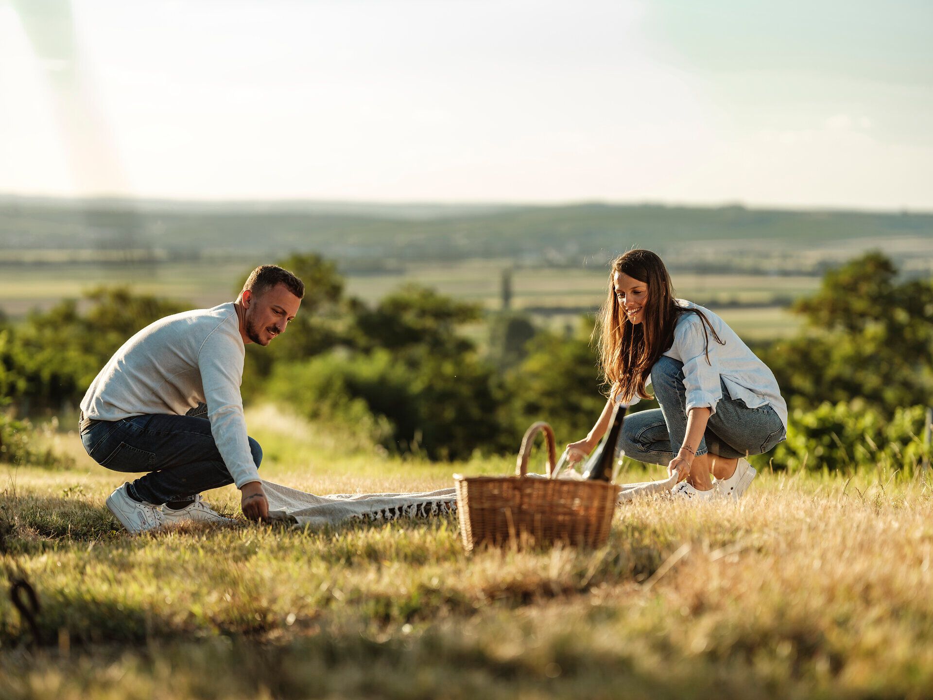 Ein romantisches Picknick im Weinviertel lädt dazu ein, die malerische Landschaft zu genießen. Umgeben von sanften Hügeln und üppigen Weinreben, breiten zwei Freunde eine Decke aus und bereiten sich darauf vor, die köstlichen Leckereien aus dem Picknickkorb zu kosten. Der Duft von frischem Wein und die warmen Sonnenstrahlen schaffen eine unvergessliche Atmosphäre.