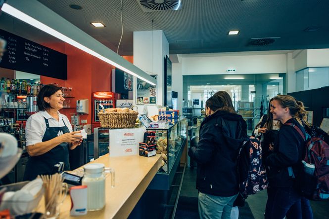 Eine Café-Mitarbeiterin bedient zwei Kundinnen an der Theke.