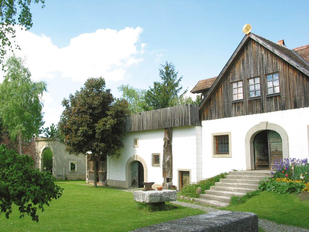 Ein traditionelles Gebäude mit Holzdach und weißer Fassade, umgeben von einem grünen Garten.