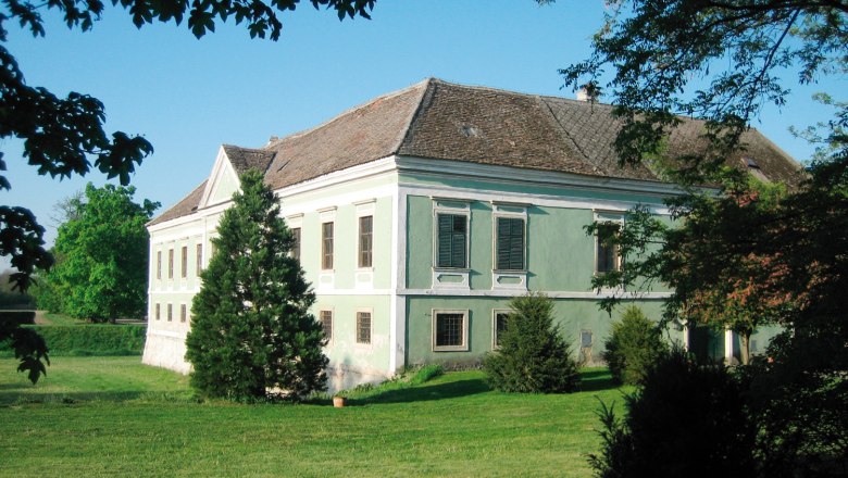 Ein altes Schloss mit grünem Anstrich und Ziegeldach, umgeben von Bäumen und Rasen.