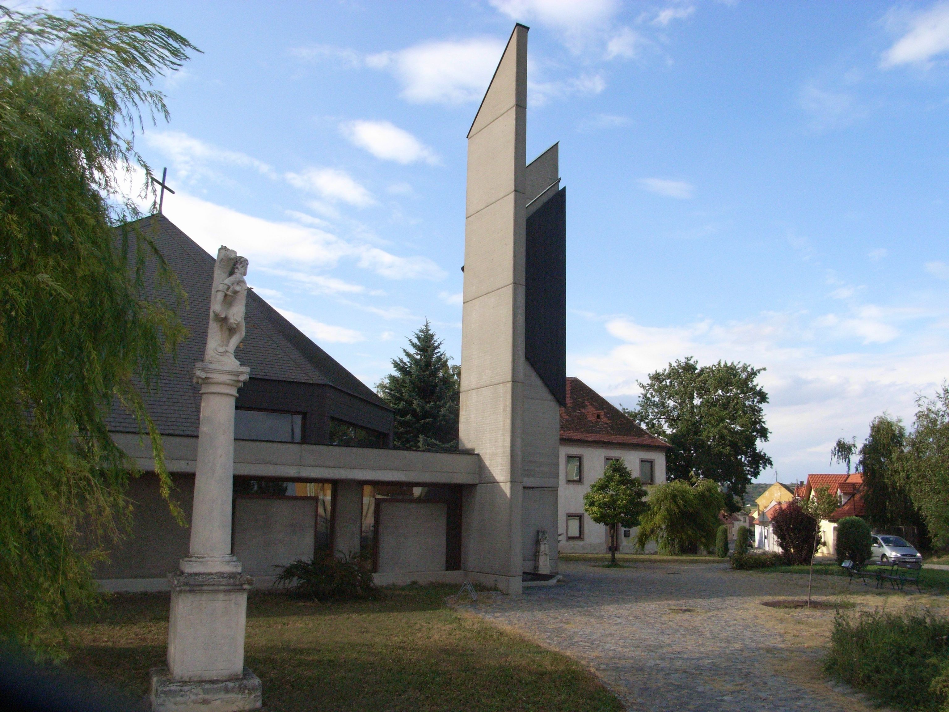 Farský kostol v Jetzelsdorfe s modernou vežou a sochou v popredí.