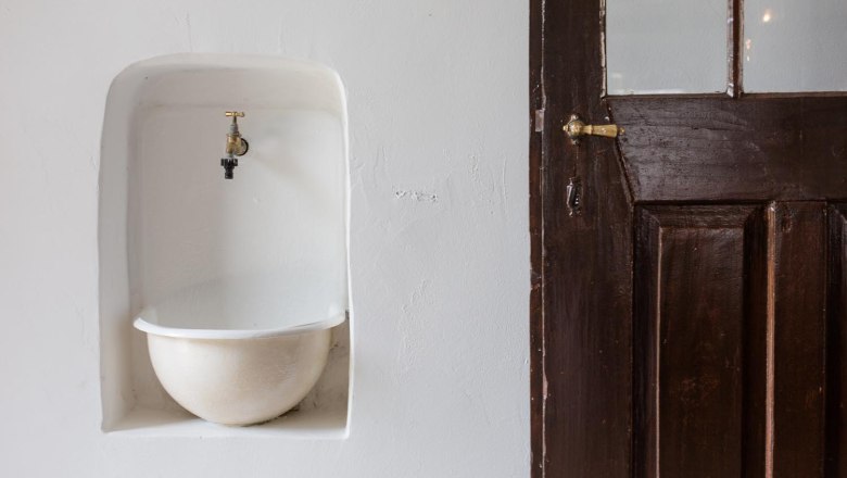 Ein alter Wasserhahn über einem eingelassenen Becken neben einer Holztür.