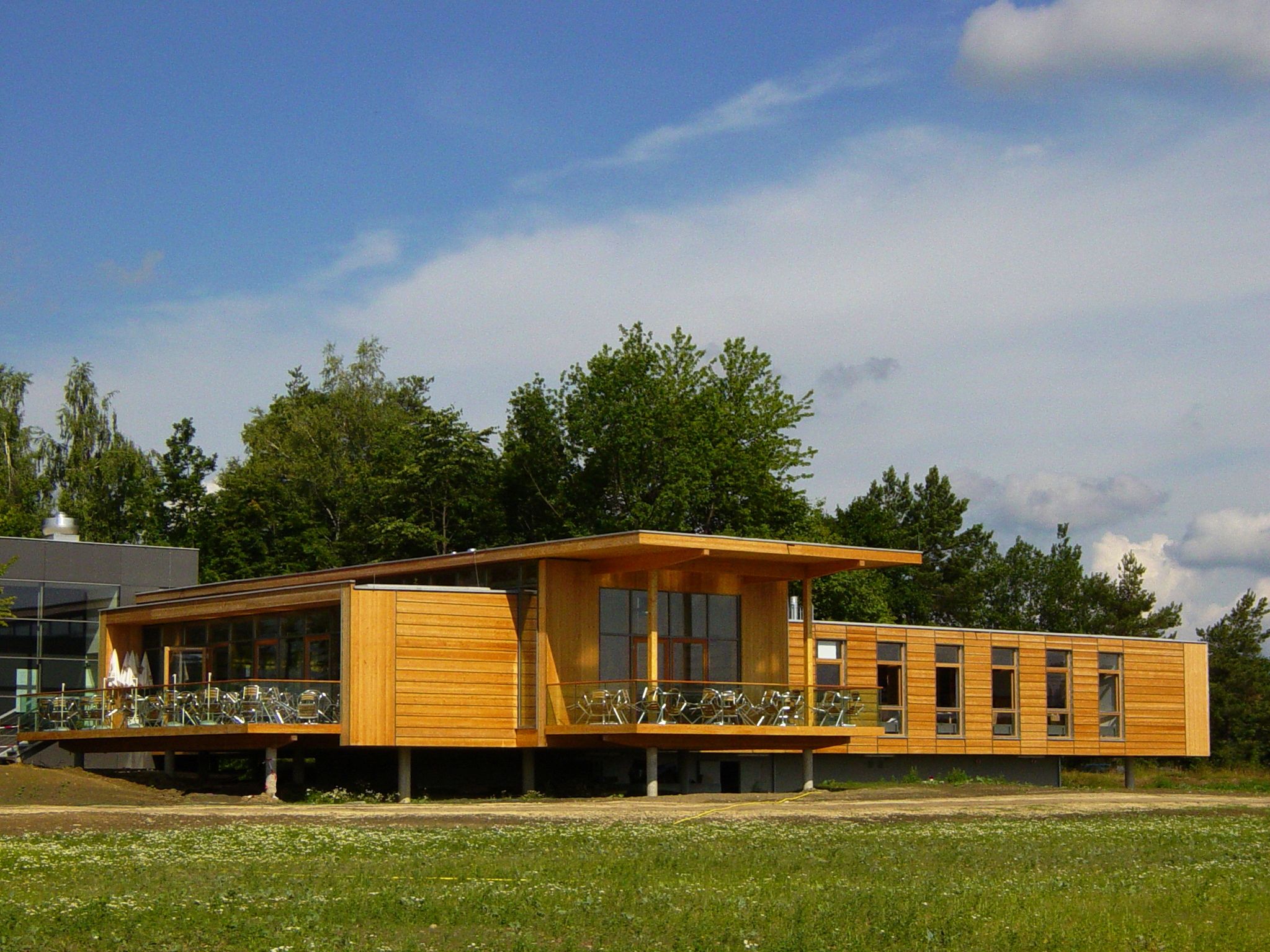 Modernes Gebäude aus Holz mit großen Fenstern und Terrasse, umgeben von Bäumen.
