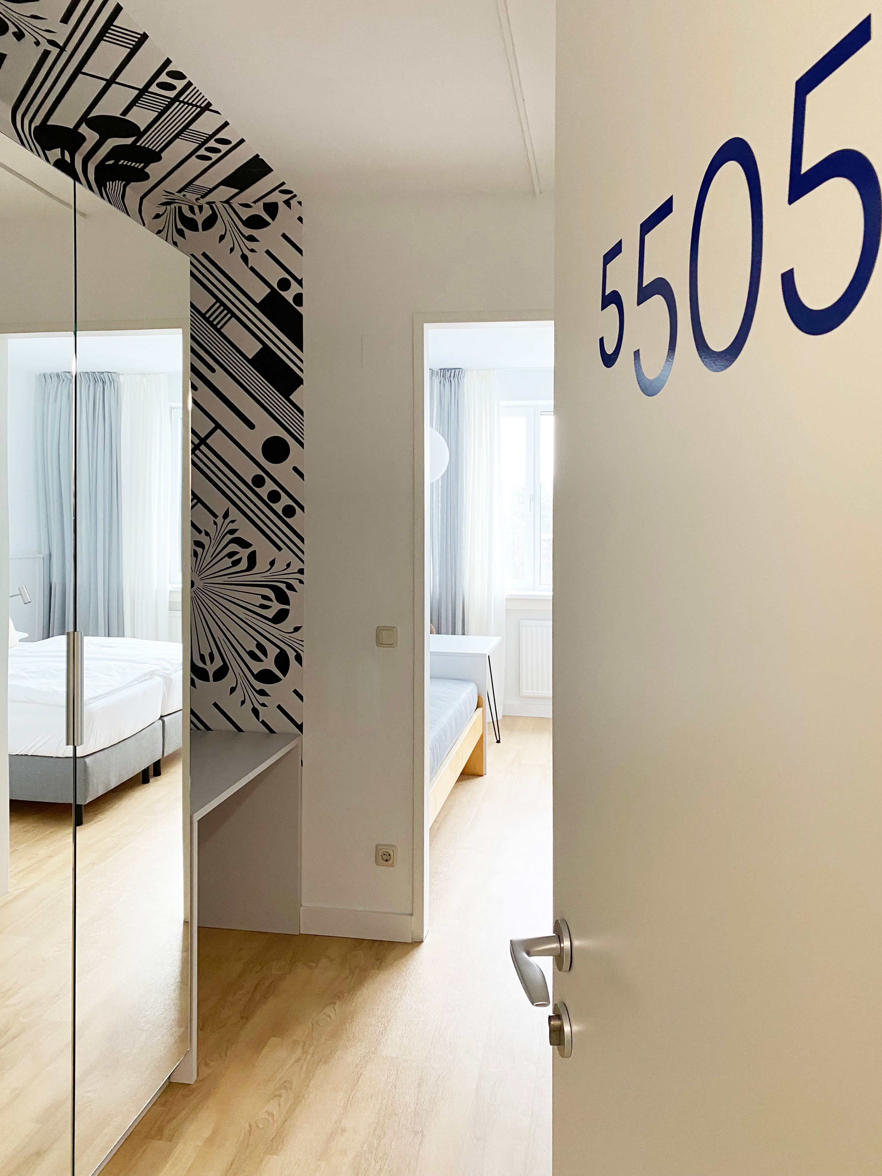 Blick in ein Gästezimmer mit der Nummer 5505, modern eingerichtet mit Bett und Spiegel.