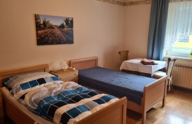 Ein einfach eingerichtetes Schlafzimmer mit zwei Einzelbetten, einem Tisch mit Stuhl und einem Fenster mit Vorhängen.