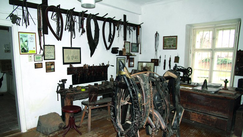 A room in a local history museum with old tools and horse harnesses on the walls.