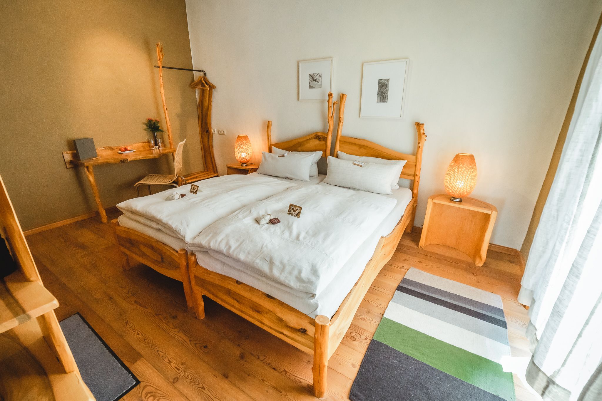 A cozy bedroom with wooden furniture, a double bed, bedside tables and a desk. Two lamps and pictures on the wall complete the ambience.