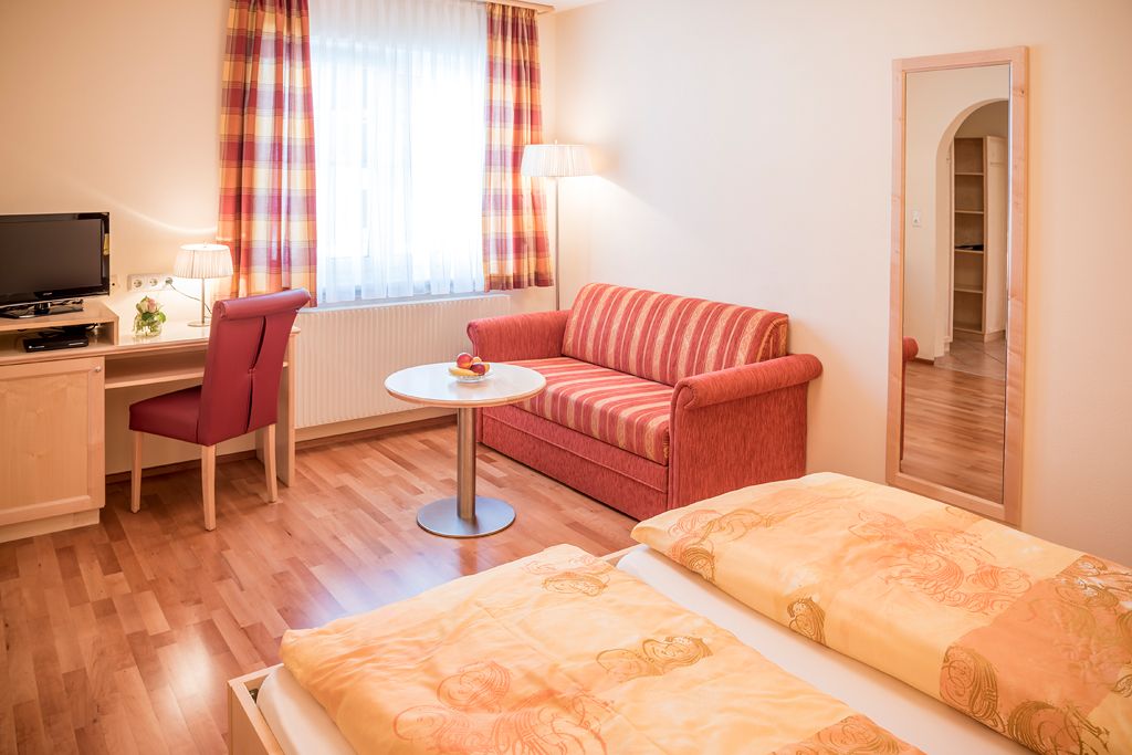 Cozy guest room with double bed, red sofa, desk, TV and large mirror.