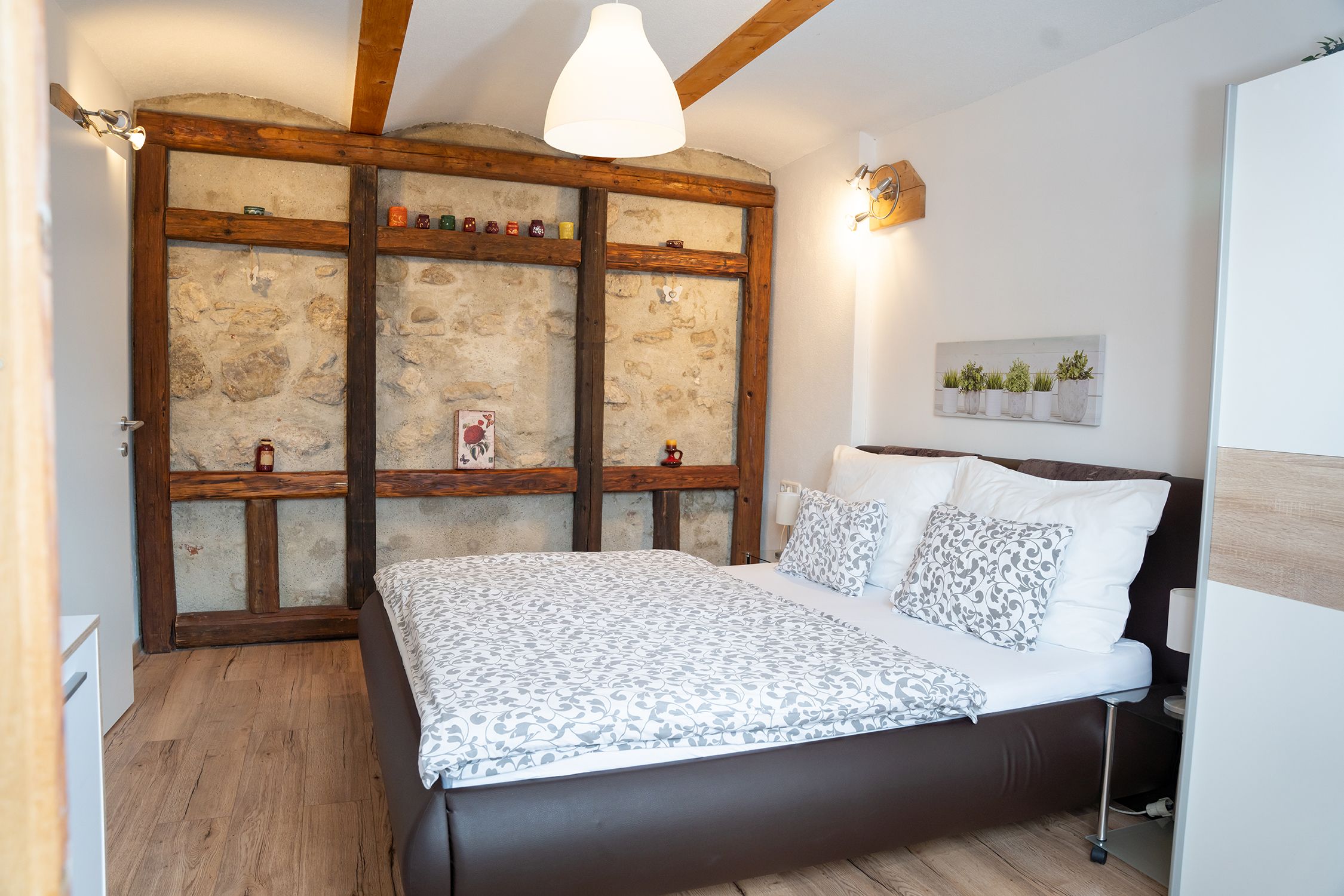 Gemütliches Schlafzimmer mit Holzbalken, Steinwand und modernem Bett.