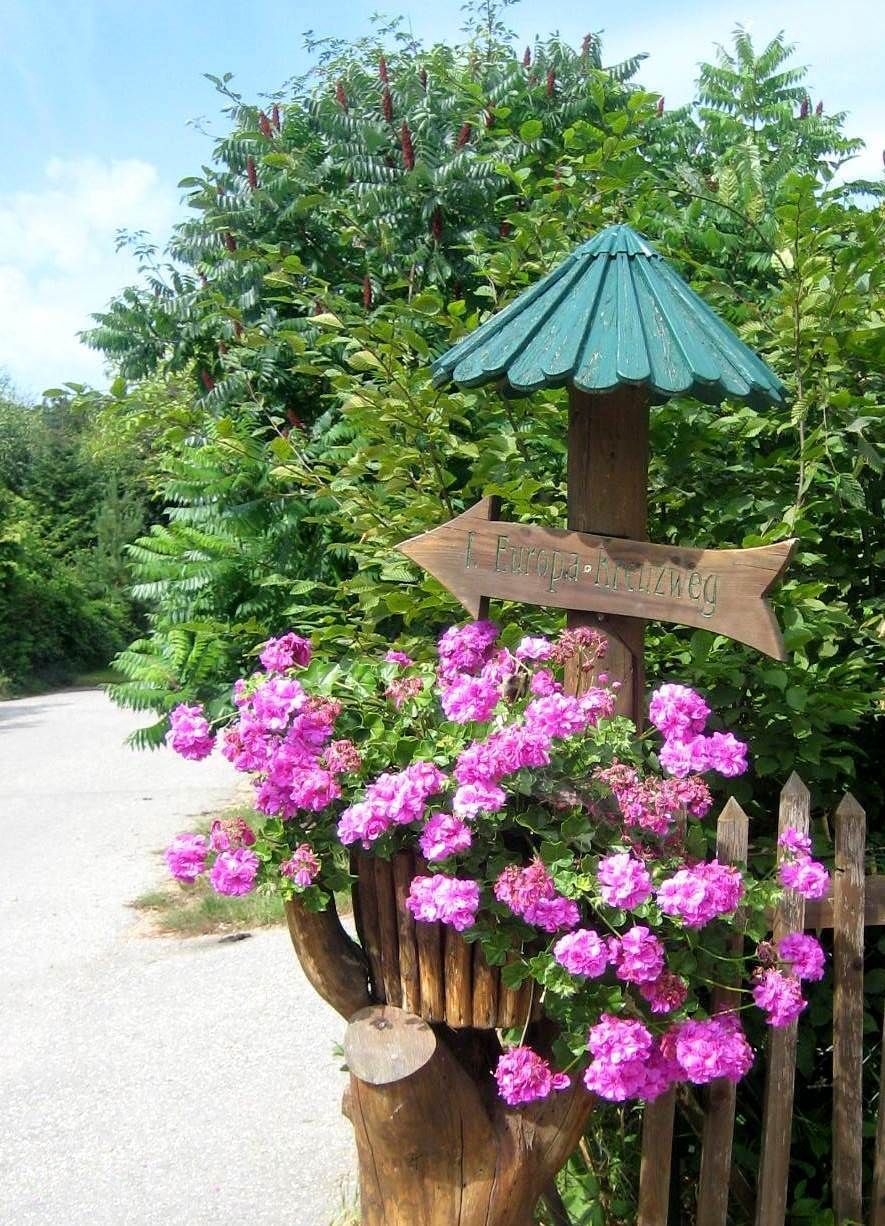 Holzschild mit Aufschrift 'Europakreuzweg' und rosa Blumen.