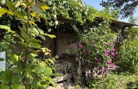 Ein bl&uuml;hender Garten mit Rosen und einer &uuml;berdachten Holzstruktur.