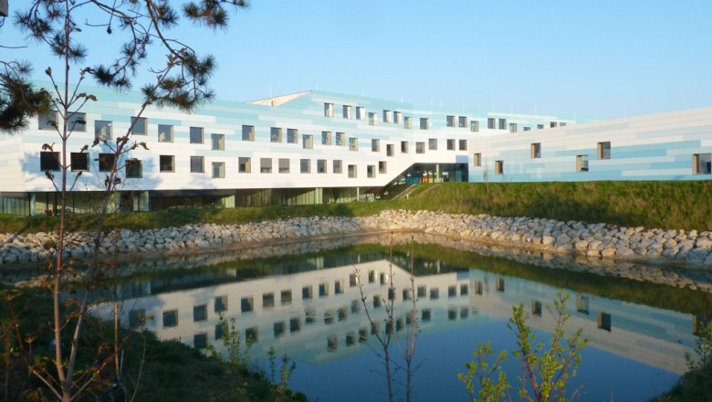 Modernes Gebäude mit blau-weißer Fassade und Teich im Vordergrund.