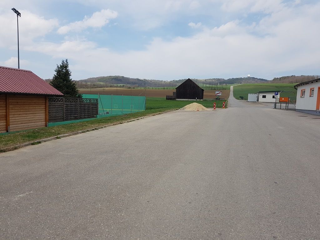 Ein leerer Parkplatz mit umliegenden Gebäuden und Feldern im Hintergrund.