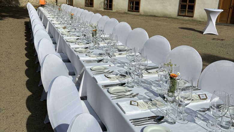 Lange, festlich gedeckte Tafel im Freien vor einem historischen Gebäude.