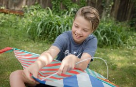 Ein Kind sitzt im Gras und hält einen bunten Drachen.