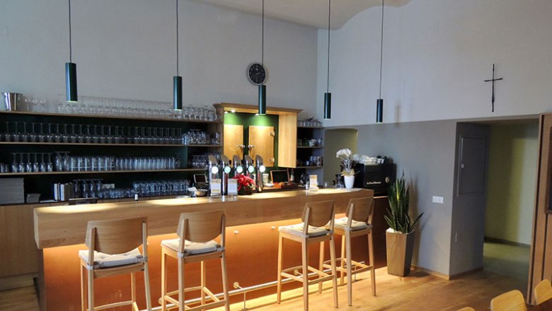 Innenansicht einer Bar mit Holztheke und Barhockern.