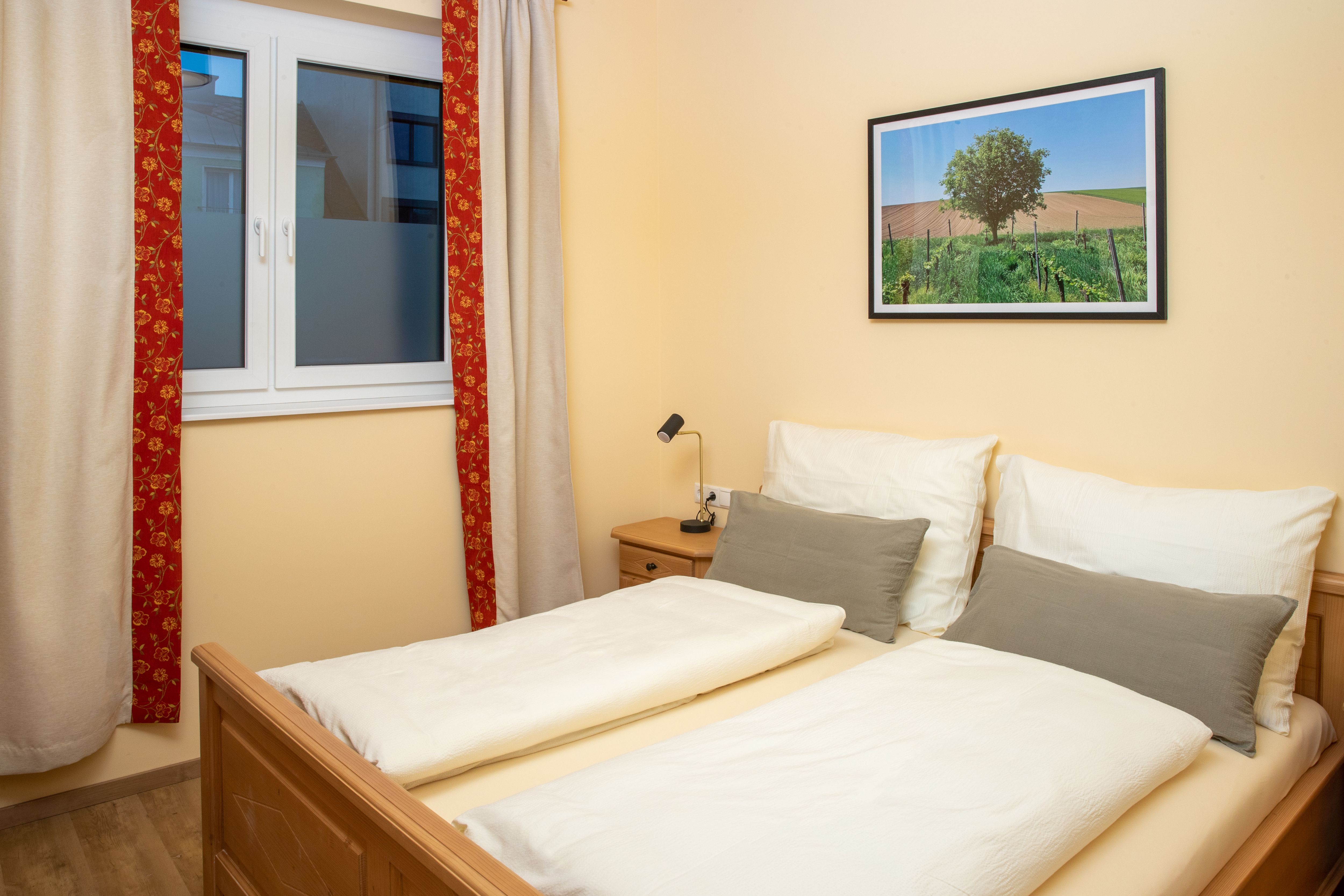 Ein gemütliches Doppelzimmer mit einem Doppelbett, einem Fenster mit Vorhängen und einem Landschaftsbild an der Wand.
