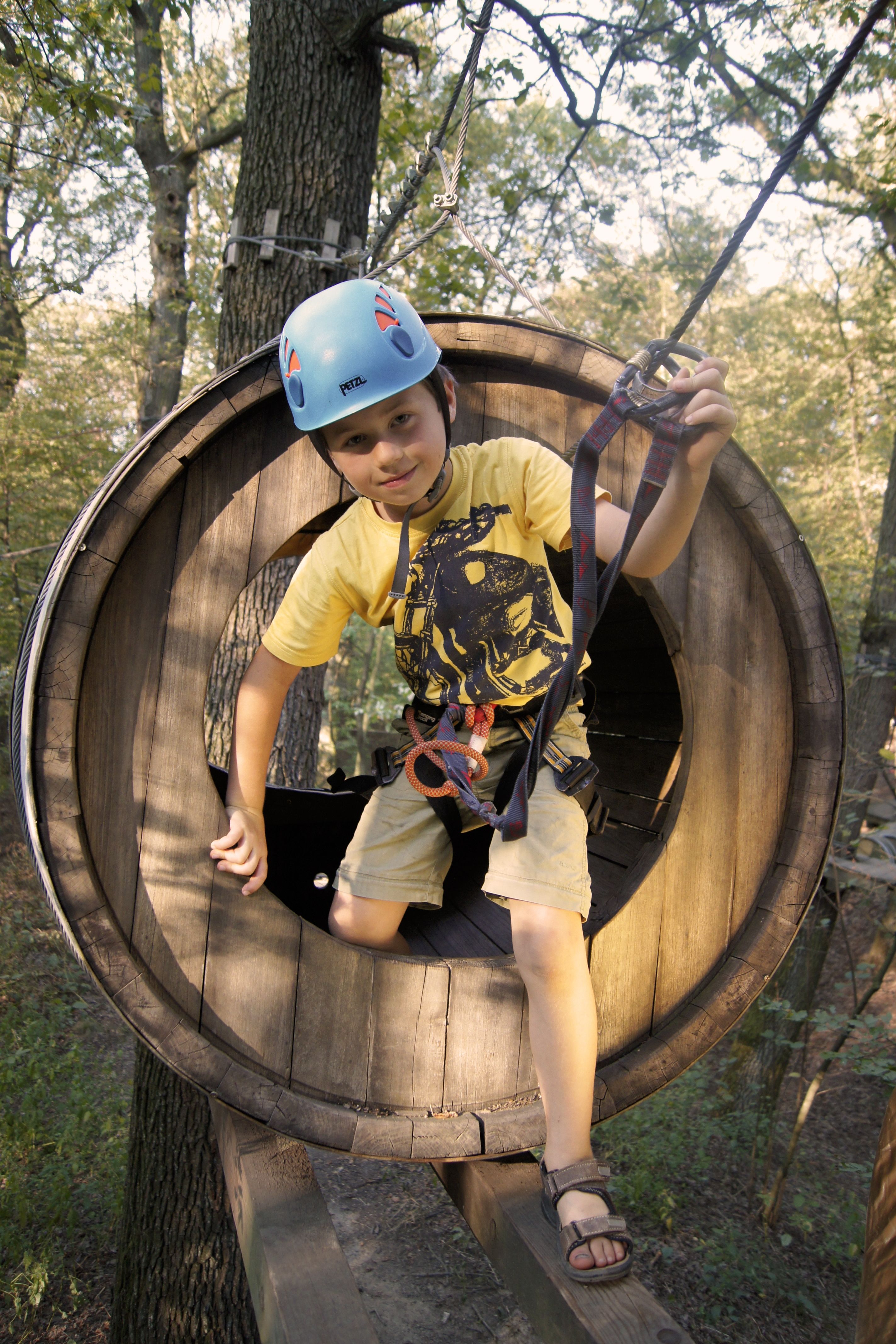 Ein Kind mit Helm und Kletterausrüstung in einem hölzernen Kletterpark-Tunnel.