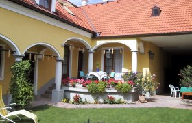 Gelbes Haus mit rotem Dach, Arkaden und Terrasse mit Blumen.