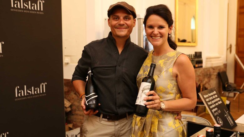 Zwei Personen halten Weinflaschen vor einem Falstaff-Poster.