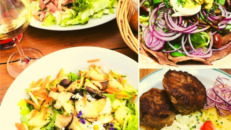 Verschiedene Teller mit Salaten, Fleisch und einem Glas Weißwein.