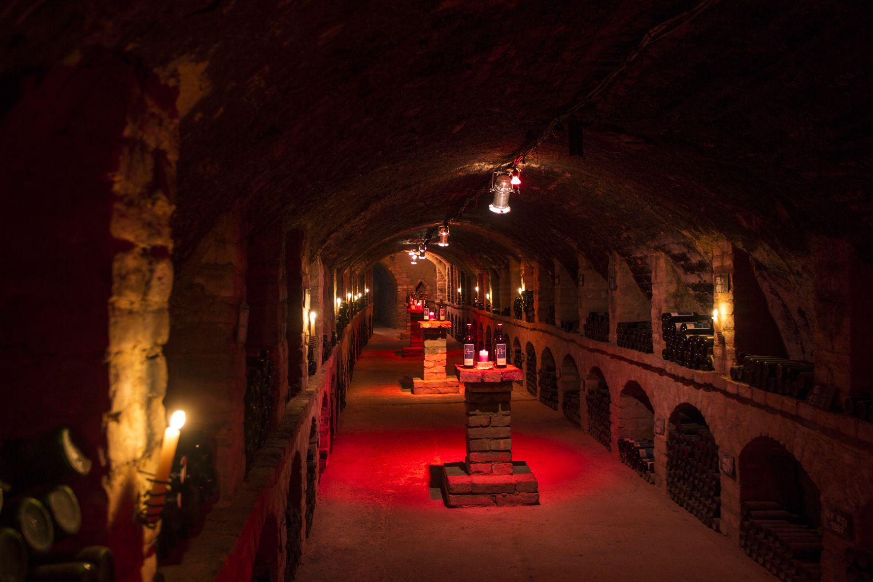 An atmospherically lit wine cellar with bottles on stone pillars.