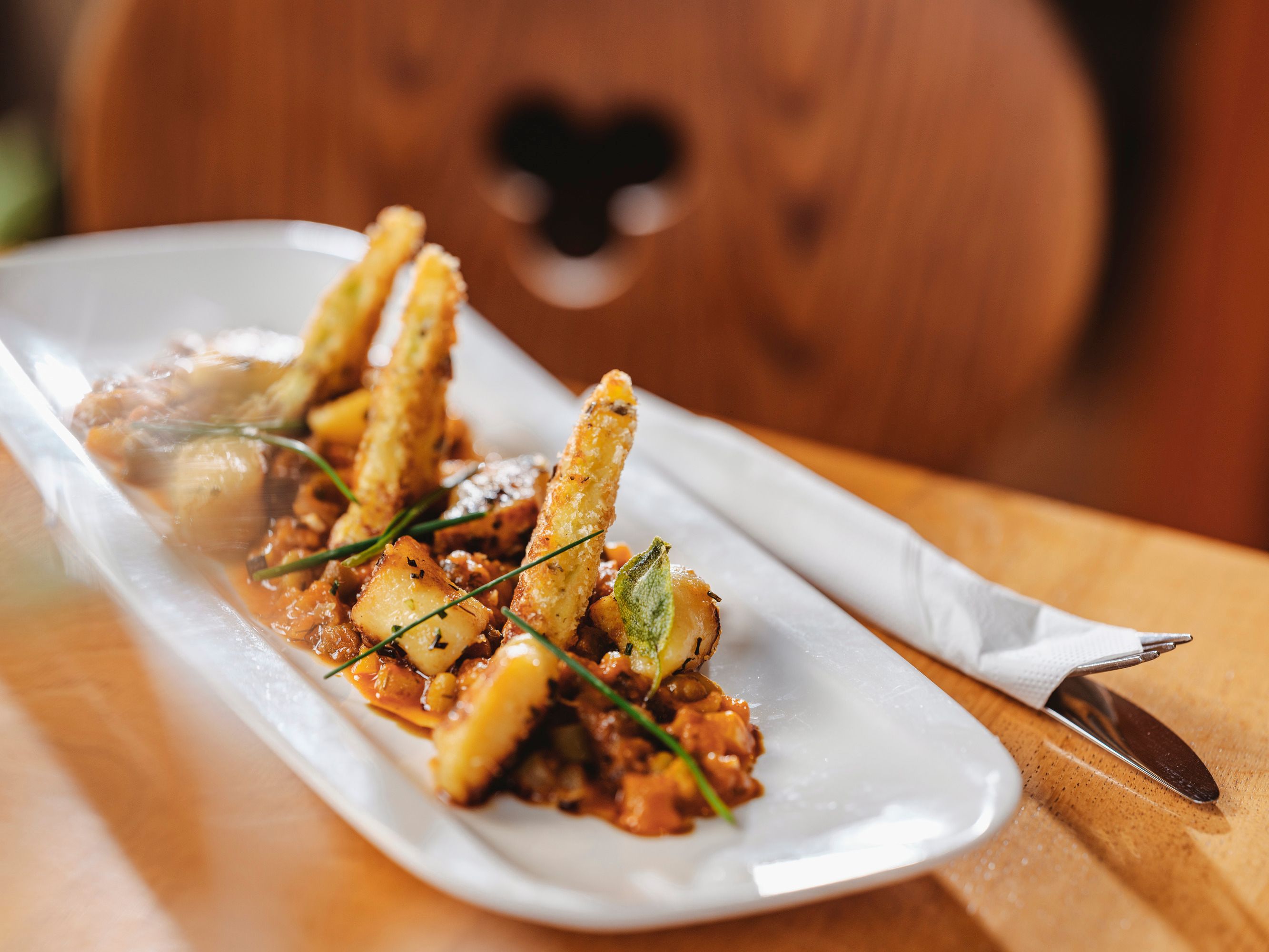Gourmetgericht auf weißem Teller mit frittierten Gemüsesticks und Kräutern.