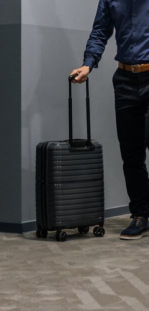 Eine junge Frau im Rollstuhl und ein Mann mit Koffer befinden sich auf dem Hotelgang am Weg zu ihrem Hotelzimmer.